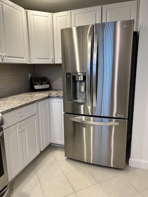 A stainless steel refrigerator with a water dispenser, a toaster, and white cabinetry in a kitchen.