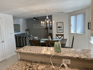 Een keuken met granieten aanrecht, een eethoek met een tafel en stoelen, een plafondventilator en een kroonluchter.