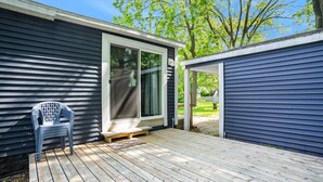 Une terrasse en bois avec une chaise en plastique, une porte-fenêtre coulissante et un espace abrité.
