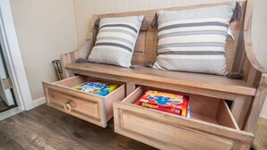 Un banc en bois avec deux coussins et deux tiroirs, dont l’un contient une boîte à jouets et l’autre un jeu de société.