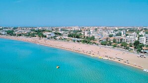 Vista aérea de una ciudad costera con una playa extensa, aguas azules cristalinas y un desarrollo urbano denso.