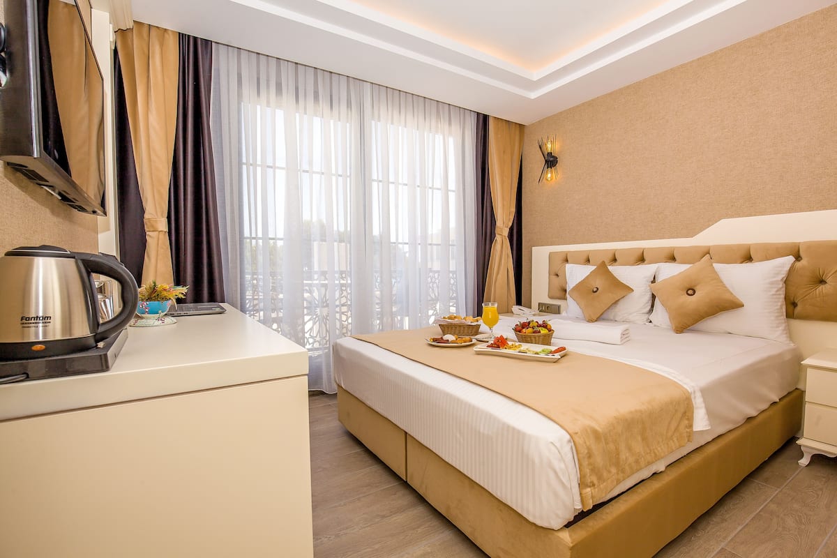 Quarto de hotel com cama, mesa de cabeceira e escrivaninha, incluindo chaleira e uma cesta de frutas.
