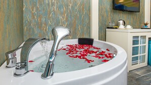 Un baño con una bañera llena de agua y pétalos de rosa, un grifo moderno y un televisor montado en la pared.