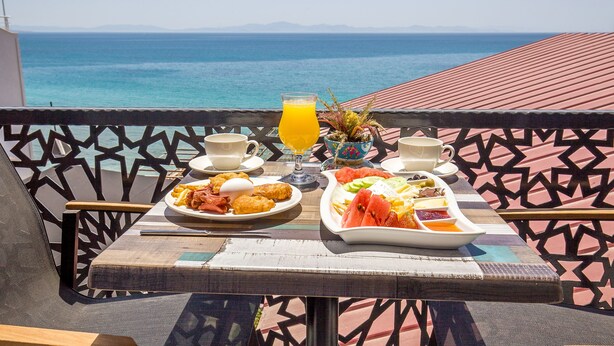 Una mesa dispuesta para el desayuno, un vaso de zumo de naranja y vista al mar.