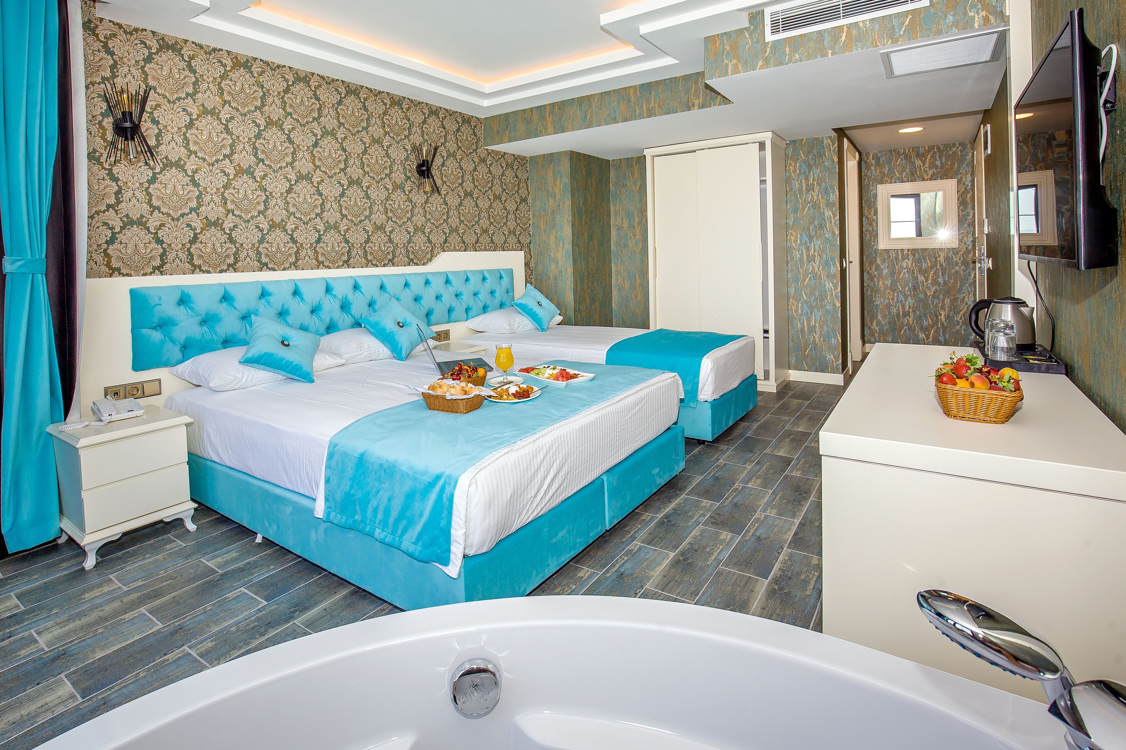 A hotel room with two beds, a large bathtub, a vanity with a mirror, and a breakfast setup.