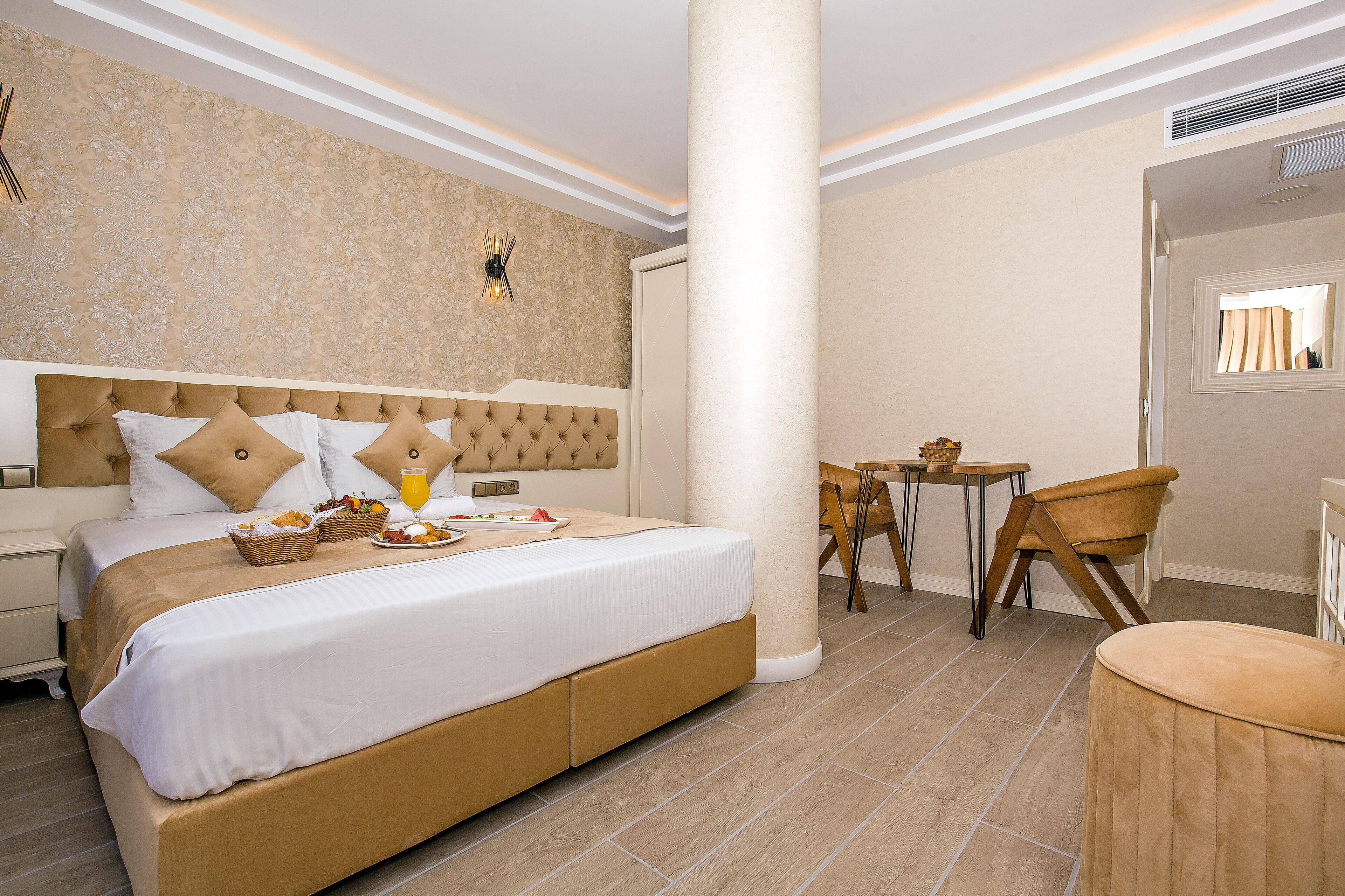 A hotel room with a large bed, a small table, a chair, and a round ottoman.