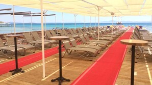 Una terraza con sillones y mesas, una alfombra roja, y vistas al mar y a las montañas.