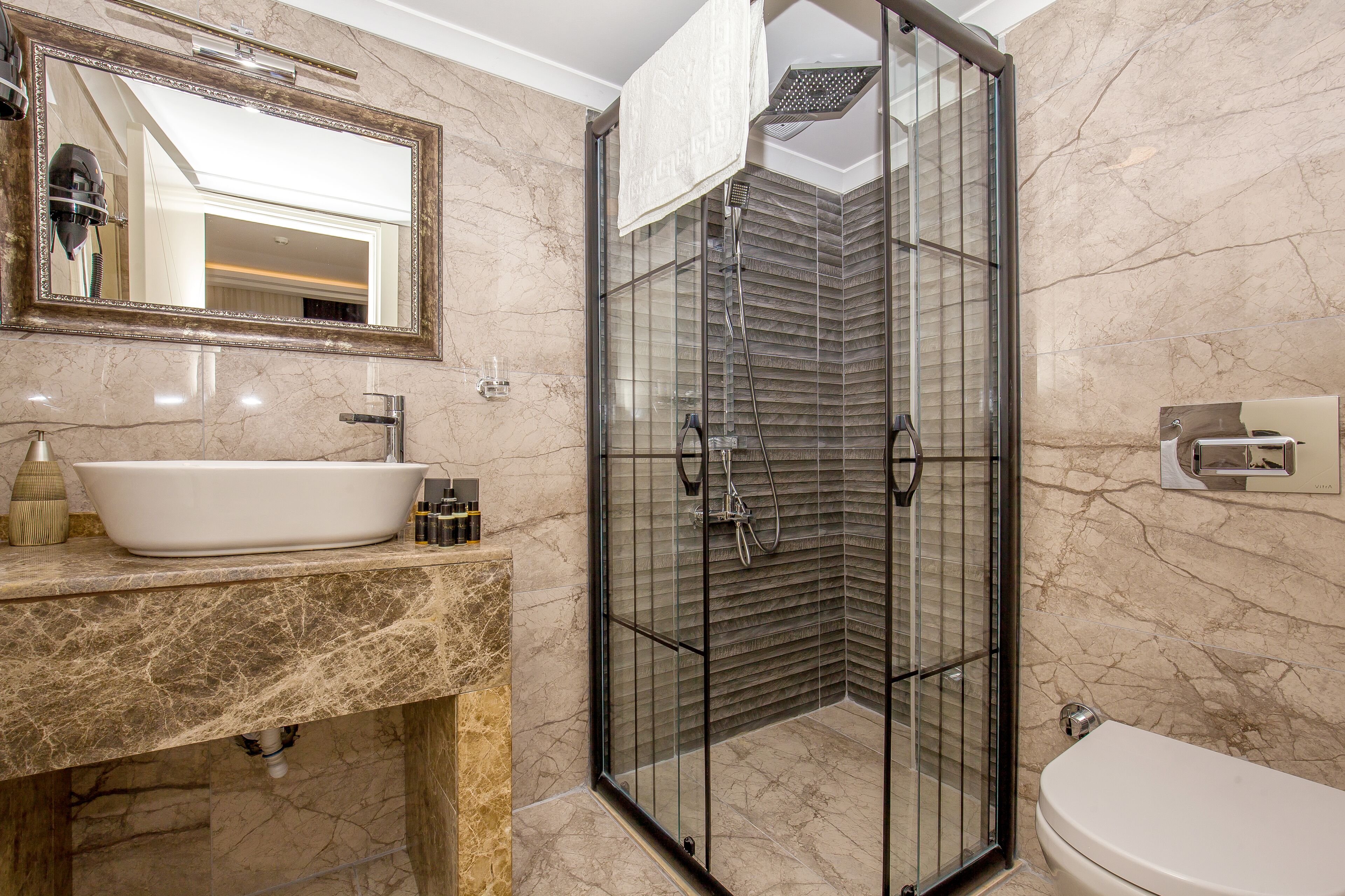 Un baño con lavamanos de mármol, ducha con cerramiento de vidrio y un inodoro.