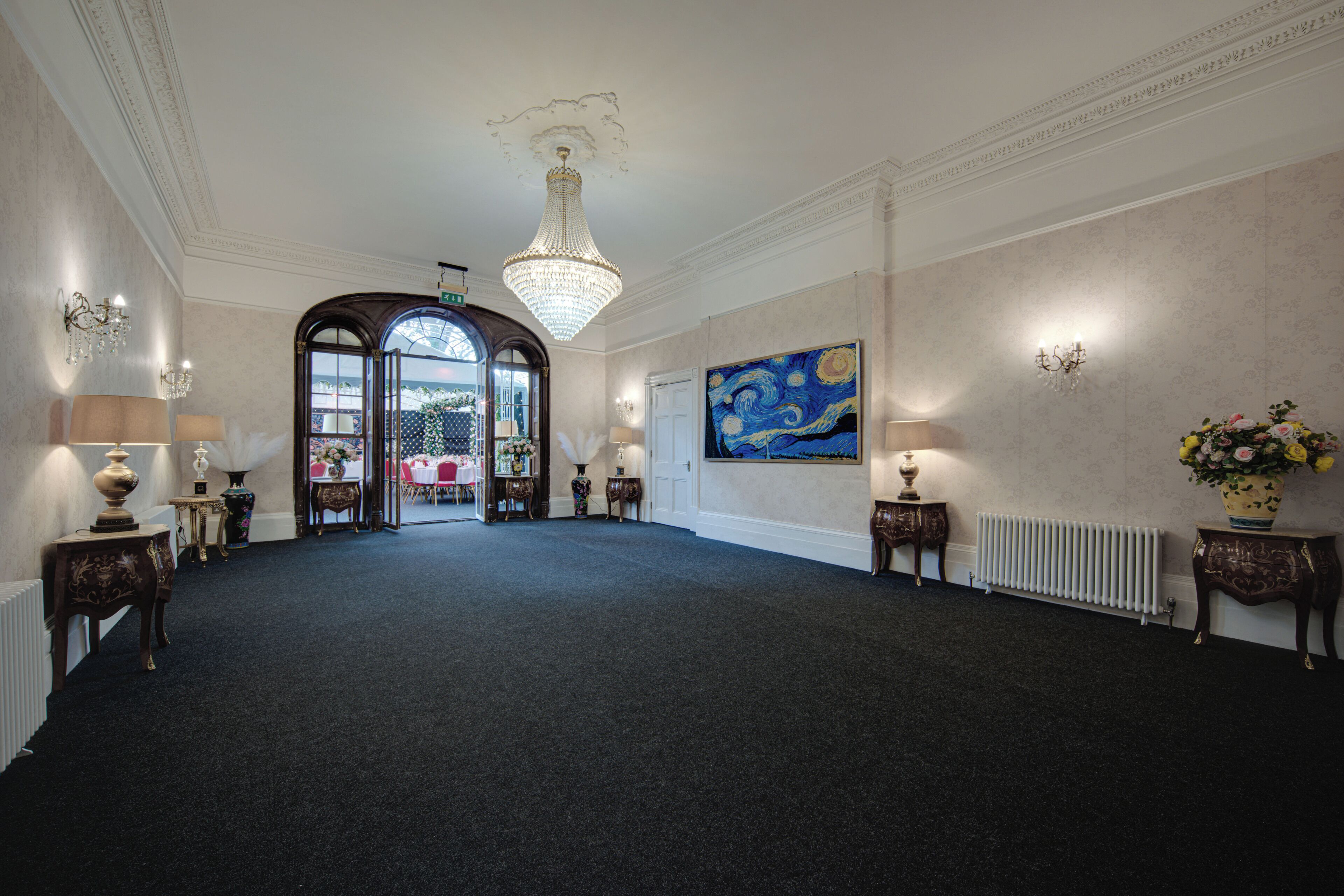 A spacious hallway with a chandelier, a large painting, and a view into a dining area.