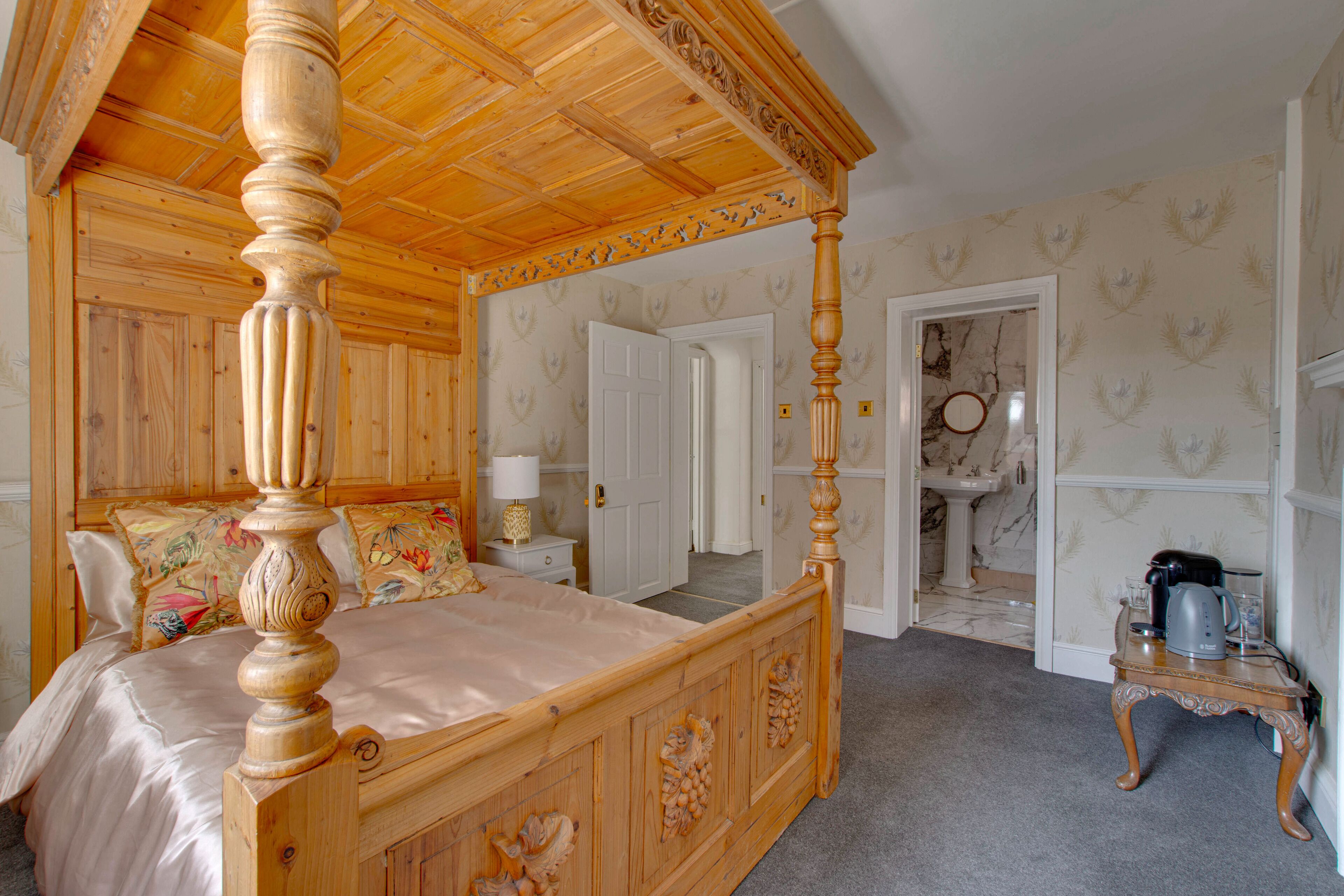 A four-poster bed with intricate carvings, a wooden ceiling, and a bathroom visible through an open door.