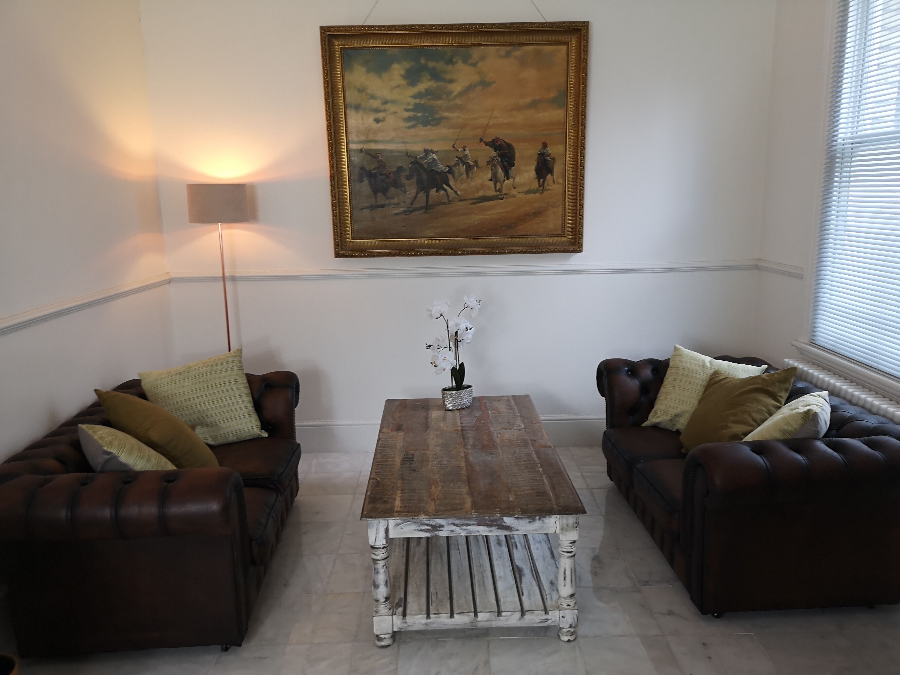 A living room with two leather sofas, a wooden coffee table, a painting, and a floor lamp.