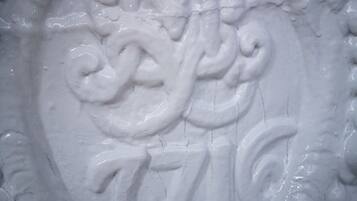 A close-up of a white, ornate architectural detail with a circular emblem and the number 7716.