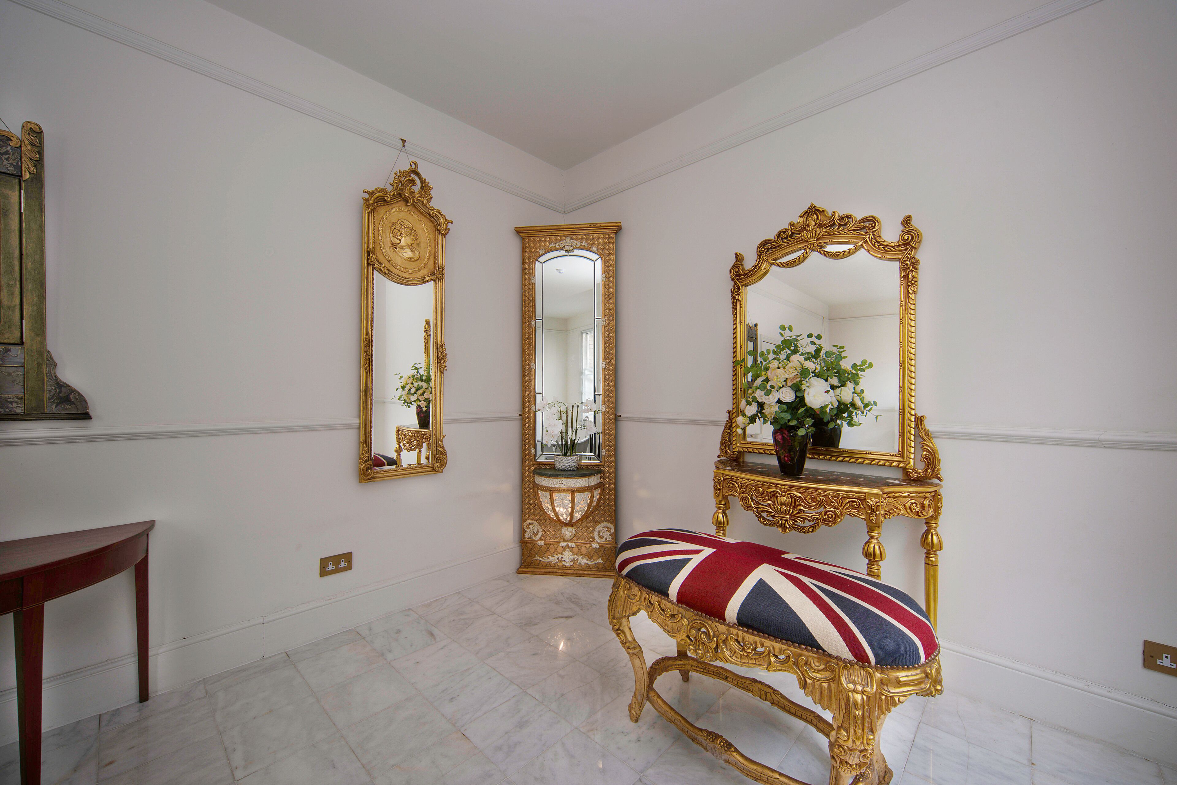 Une pièce dotée d’un sol en marbre, d’un banc agrémenté d’un coussin orné de l’Union Jack, et de deux miroirs décoratifs accrochés aux murs.