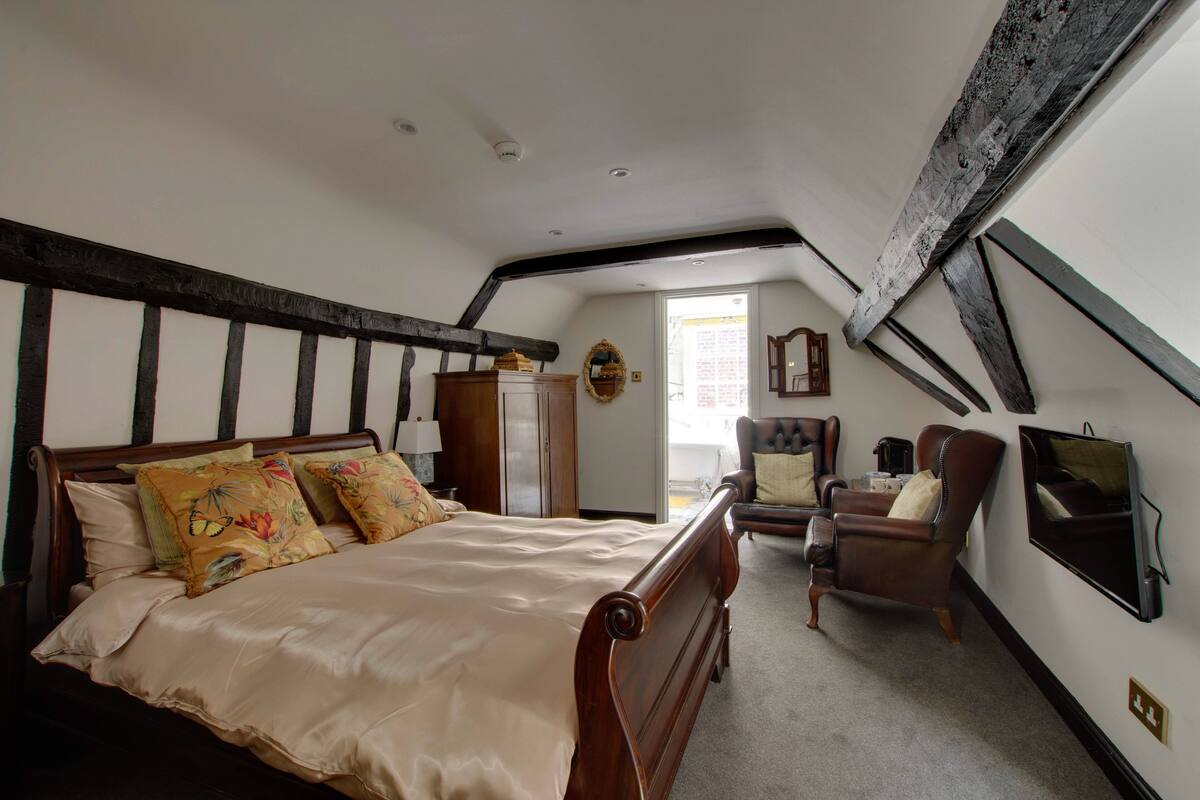 Ein Schlafzimmer mit einem großen Bett, einem Sessel, einem Fernseher und einem Fenster.
