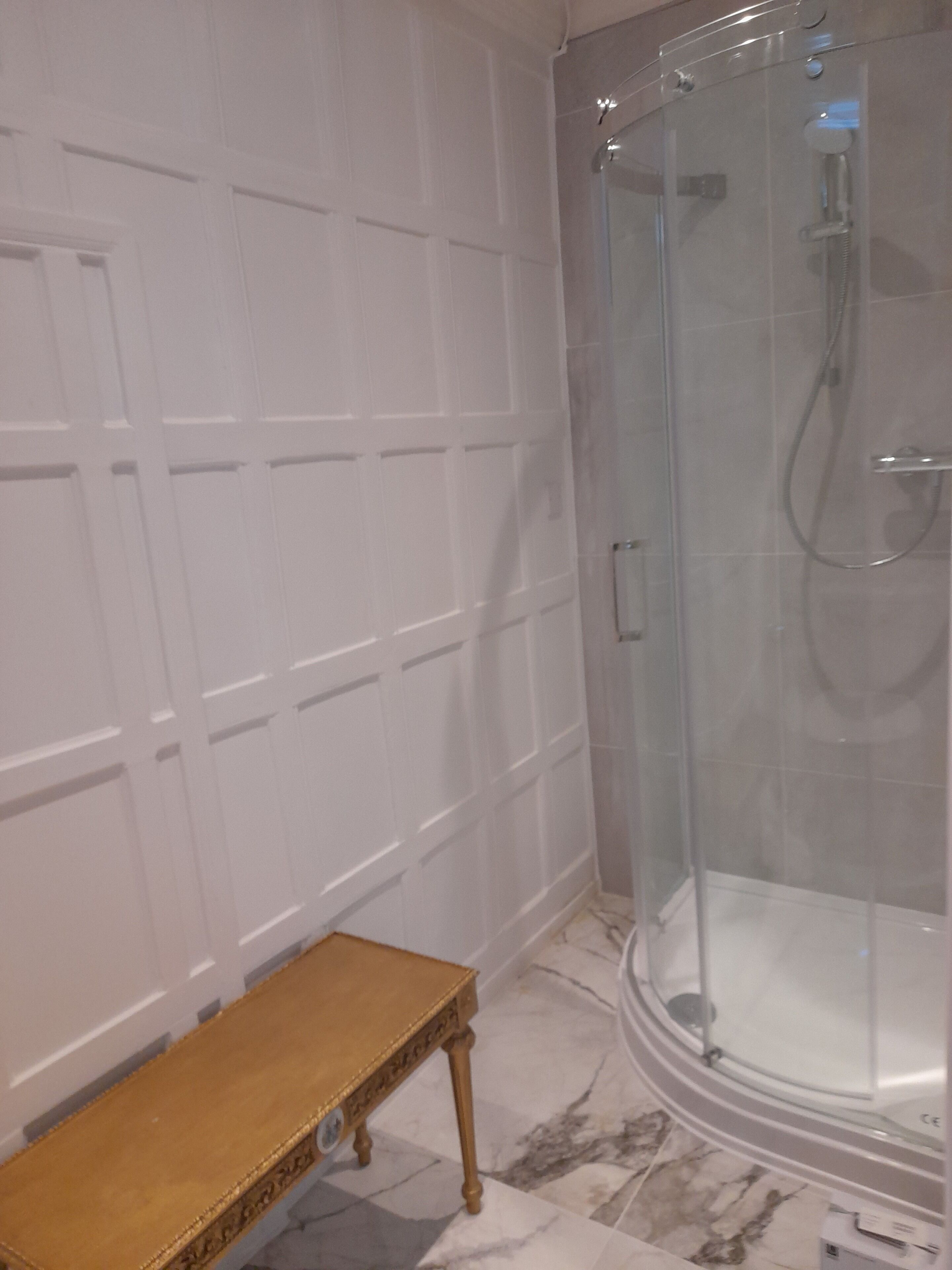 A bathroom with a glass shower enclosure, a wooden bench, and a tiled floor.