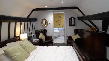 A bedroom with a large bed, two armchairs, a dresser, and a mirror on the wall.