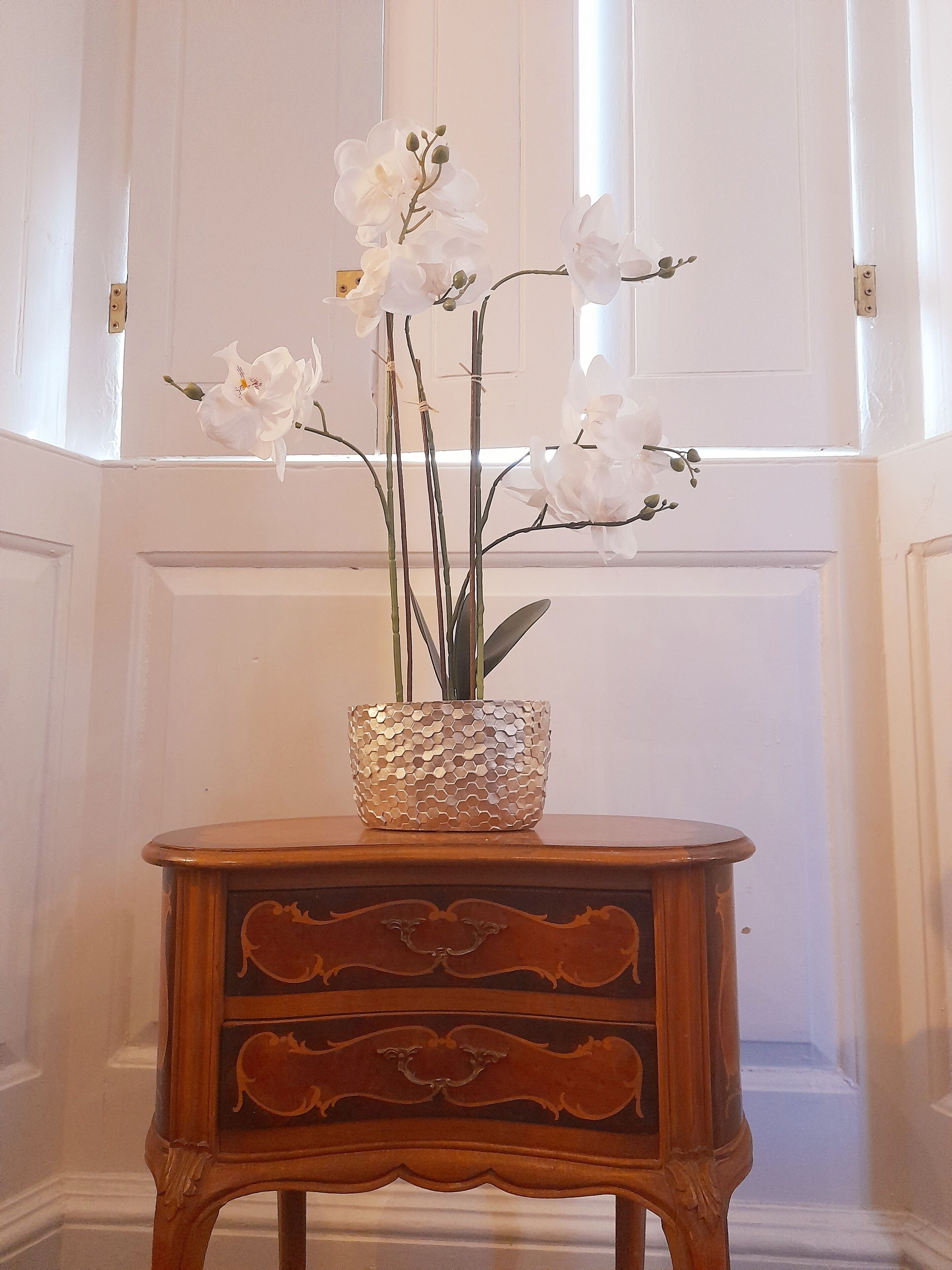 A wooden side table with a textured, hexagonal vase containing white orchids.
