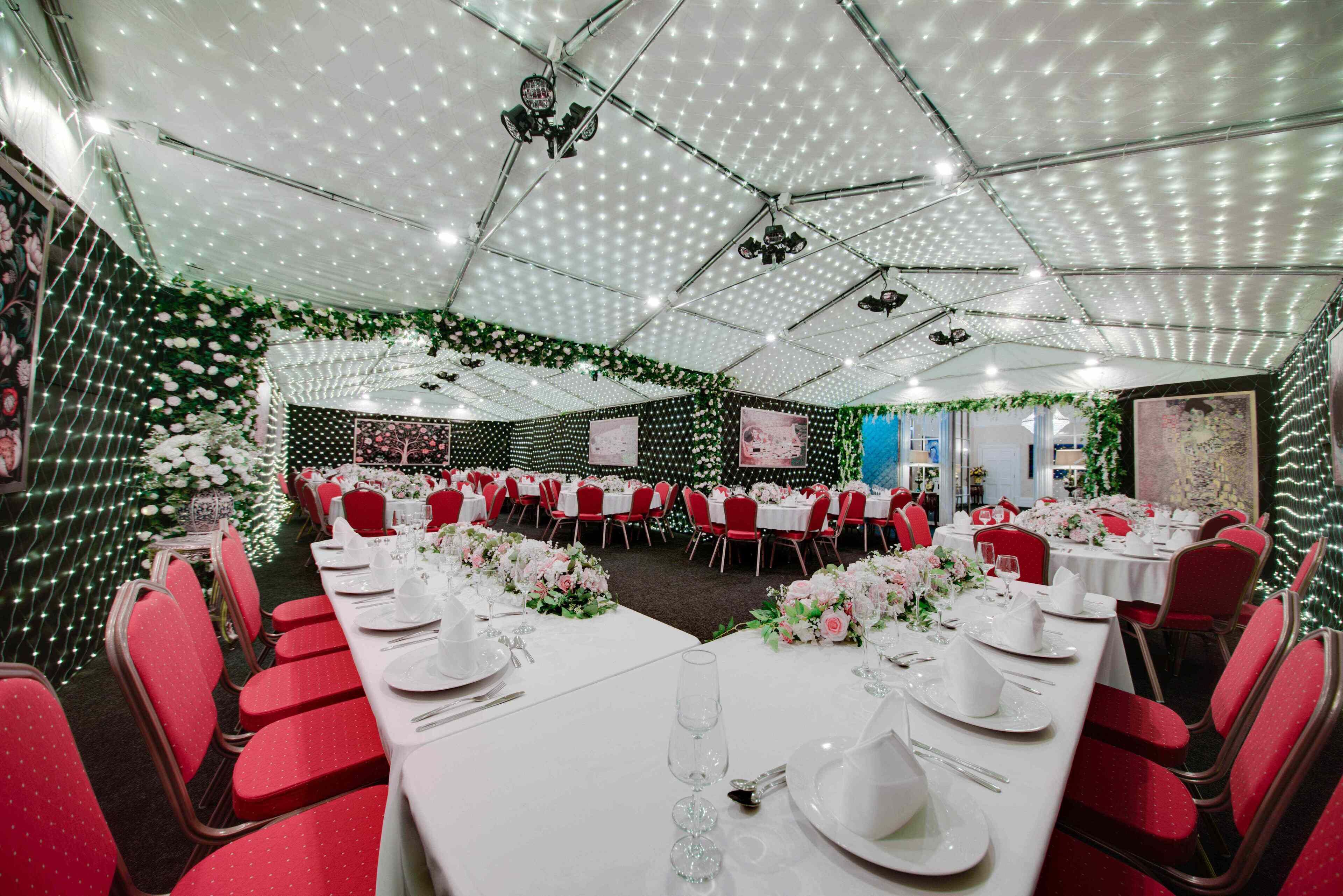 A banquet hall with round tables, red chairs, and white tablecloths.