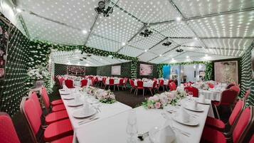 A banquet hall with round tables, red chairs, and white tablecloths.