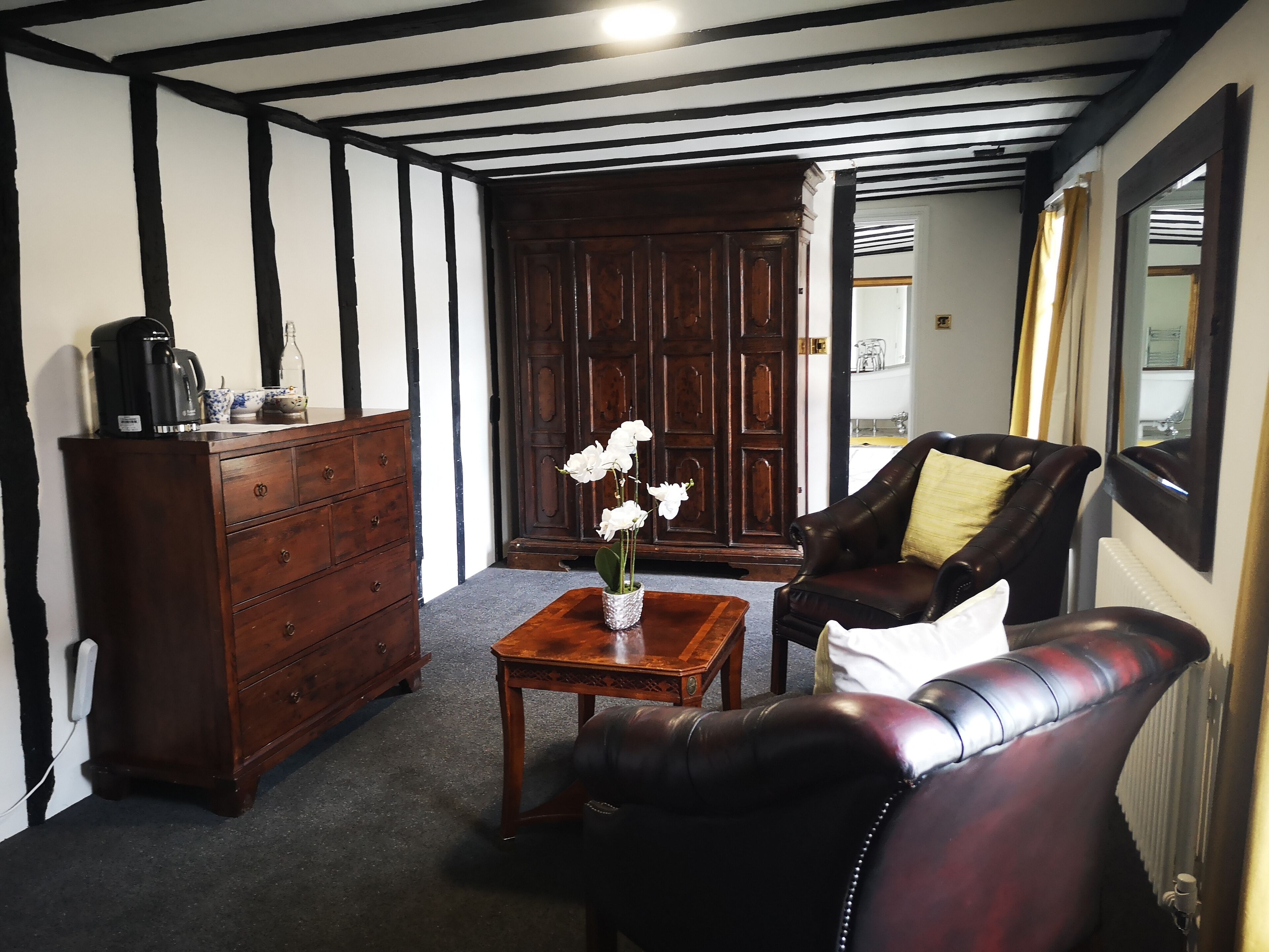 Una habitación con un mueble de madera oscura, un sofá de cuero, una mesa de centro de madera con un jarrón de flores blancas y una puerta de madera grande.