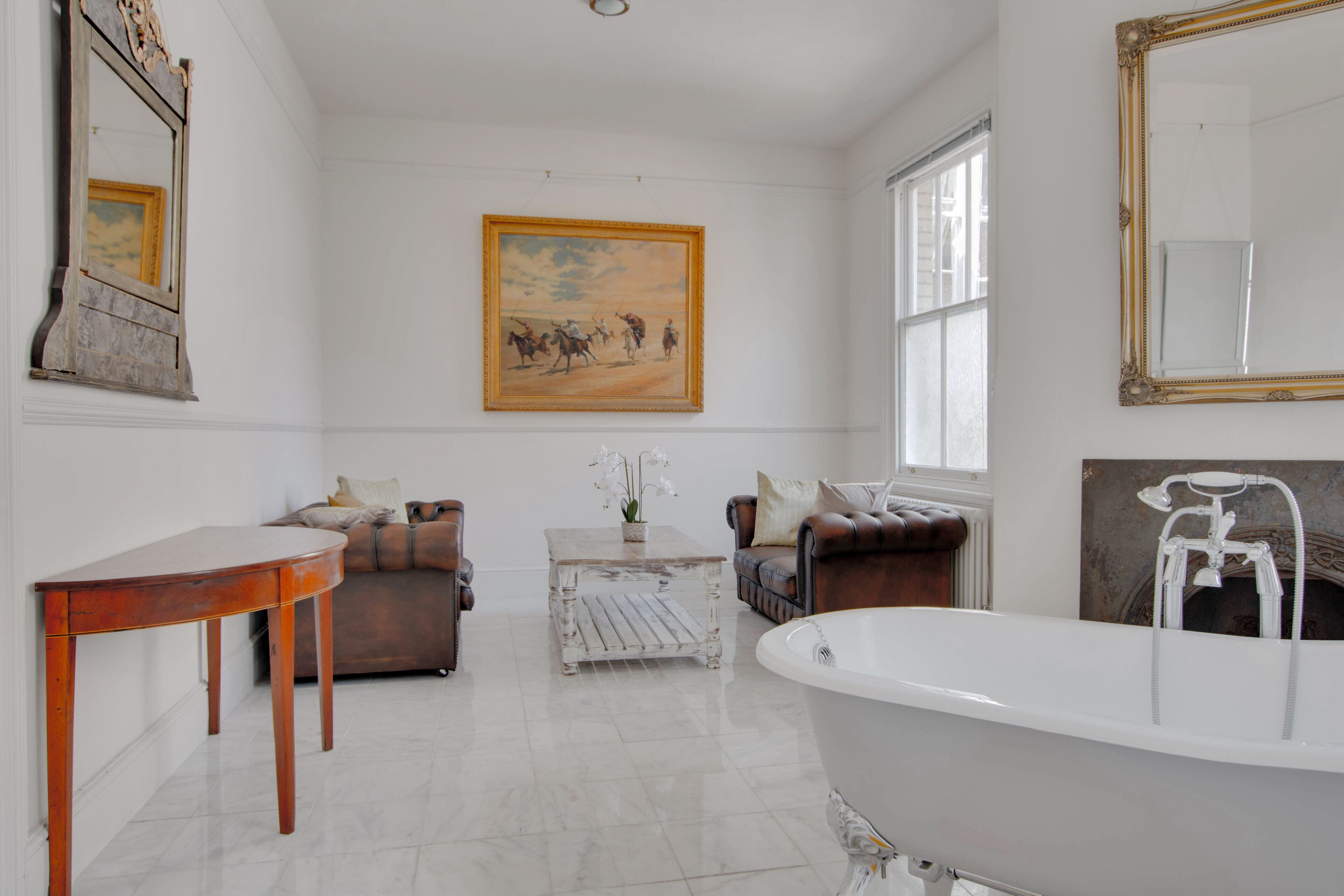 Un baño amplio con una bañera grande, un tocador de madera, un sofá de cuero marrón y un cuadro en la pared.