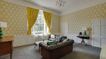 A room with a brown leather sofa, a wooden table, a radiator, and a window with yellow curtains.