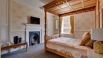 A bedroom with a four-poster bed, a fireplace, a television, and a window with curtains.