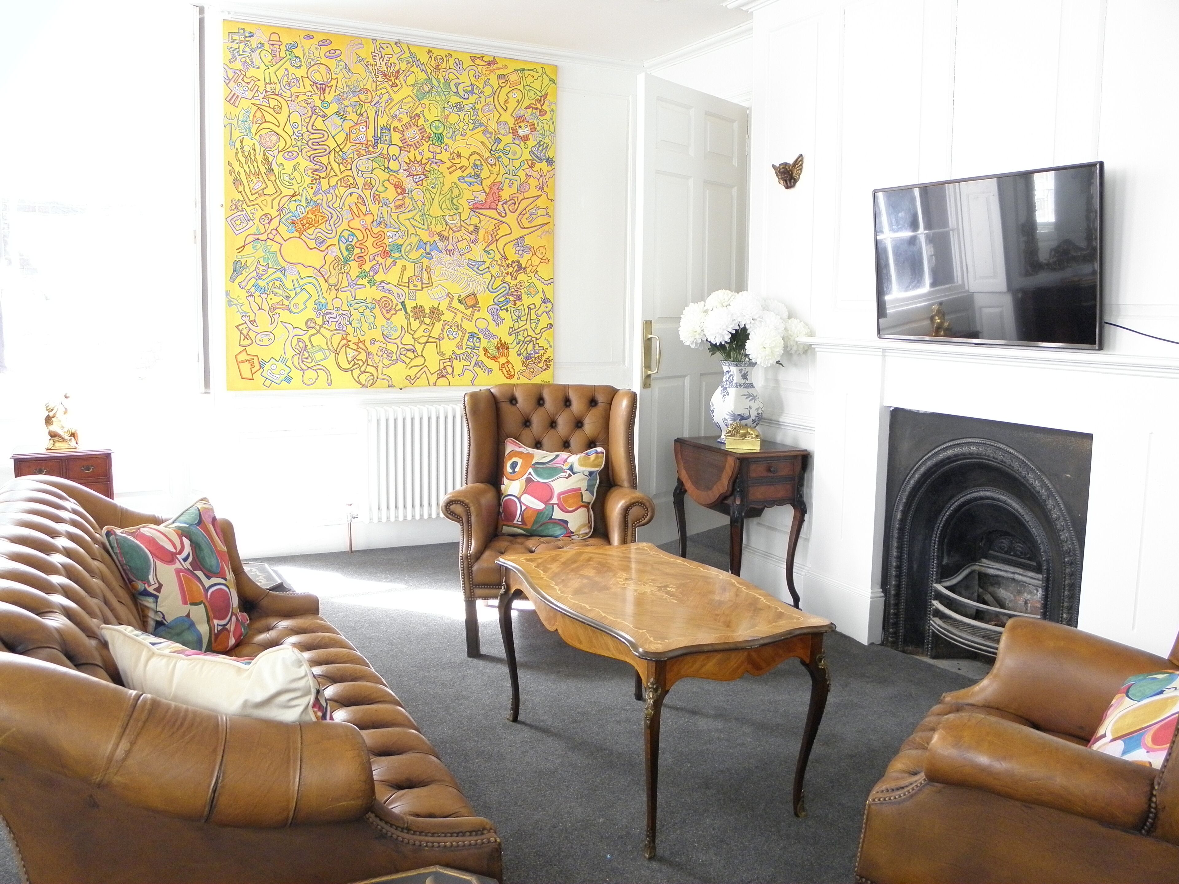 A living room with a brown leather sofa, a wooden coffee table, a large abstract painting, a television, and a fireplace.
