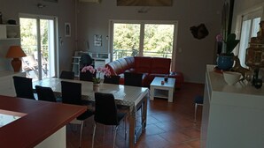 A modern kitchen with a dining area, a red sofa, and a balcony with a view of greenery. - VILLA WITH HEATED SWIMMING POOL JACCUZI SAUNA (Barjac)