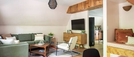 Un salon chaleureux avec un canapé vert, une table basse en bois et un coin repas comprenant une table et des chaises.