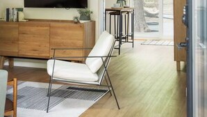 Una sala de estar moderna con techo de madera, un televisor de pantalla plana grande, un sillón de cuero blanco y una mesita con una planta.