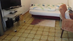 Ein Zimmer mit einem Bett, einem Fernseher auf einem Schrank, einem Tisch und einem Stuhl.