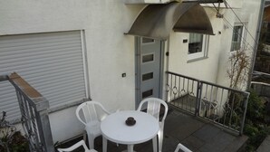 Eine kleine Terrasse im Freien mit einem runden Tisch und vier weißen Plastikstühlen.