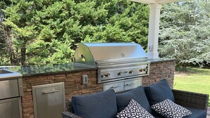 En udendørs terrasse med en sten grill, fletningsmøbler og en tæppe med mønster.