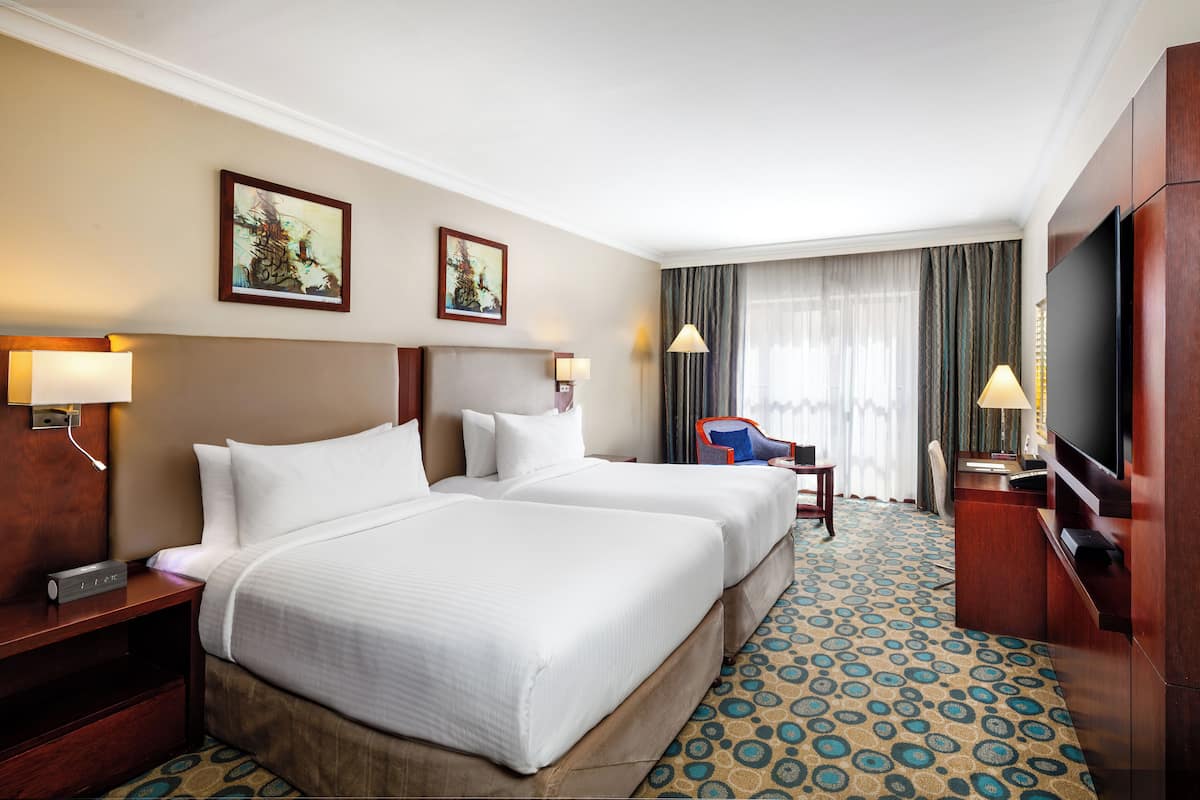 Une chambre d’hôtel avec deux lits, un bureau, une télévision et une grande fenêtre avec des rideaux.