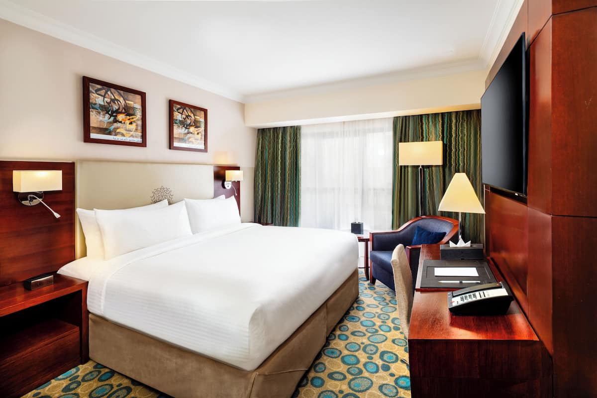 Une chambre d’hôtel avec un grand lit, un bureau avec une lampe, une télévision et des œuvres d’art accrochées aux murs.