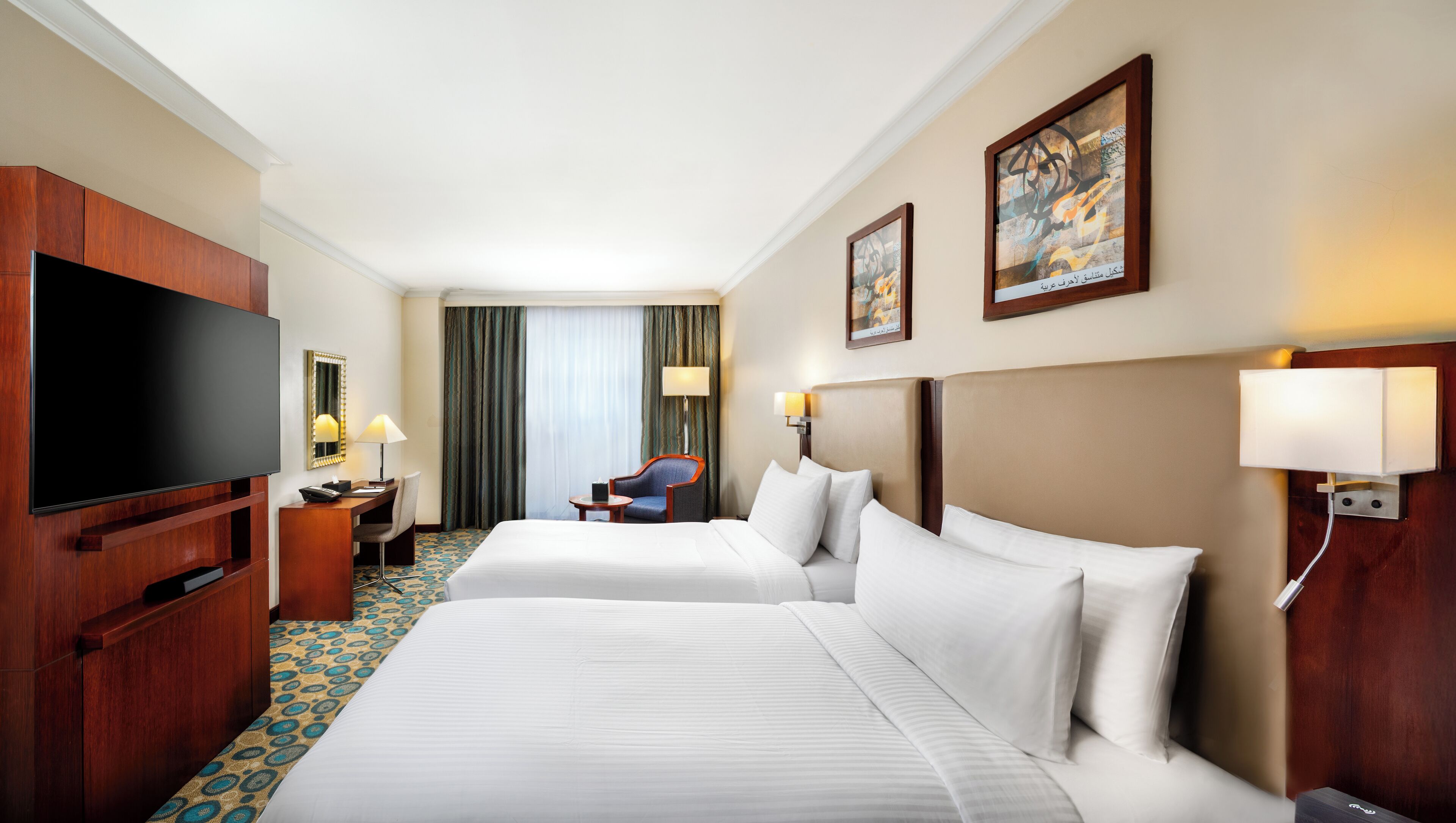 A hotel room with two beds, a TV, a desk, a chair, and a large window with curtains.