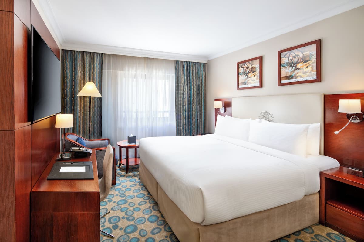 Une chambre d’hôtel avec un grand lit, un bureau doté d’un téléviseur à écran plat, une lampe et une petite table sur laquelle est posée une bougie.