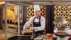 Een kok bereidt eten toe aan een buffet met een decoratieve achtergrond en een grote kookpot.