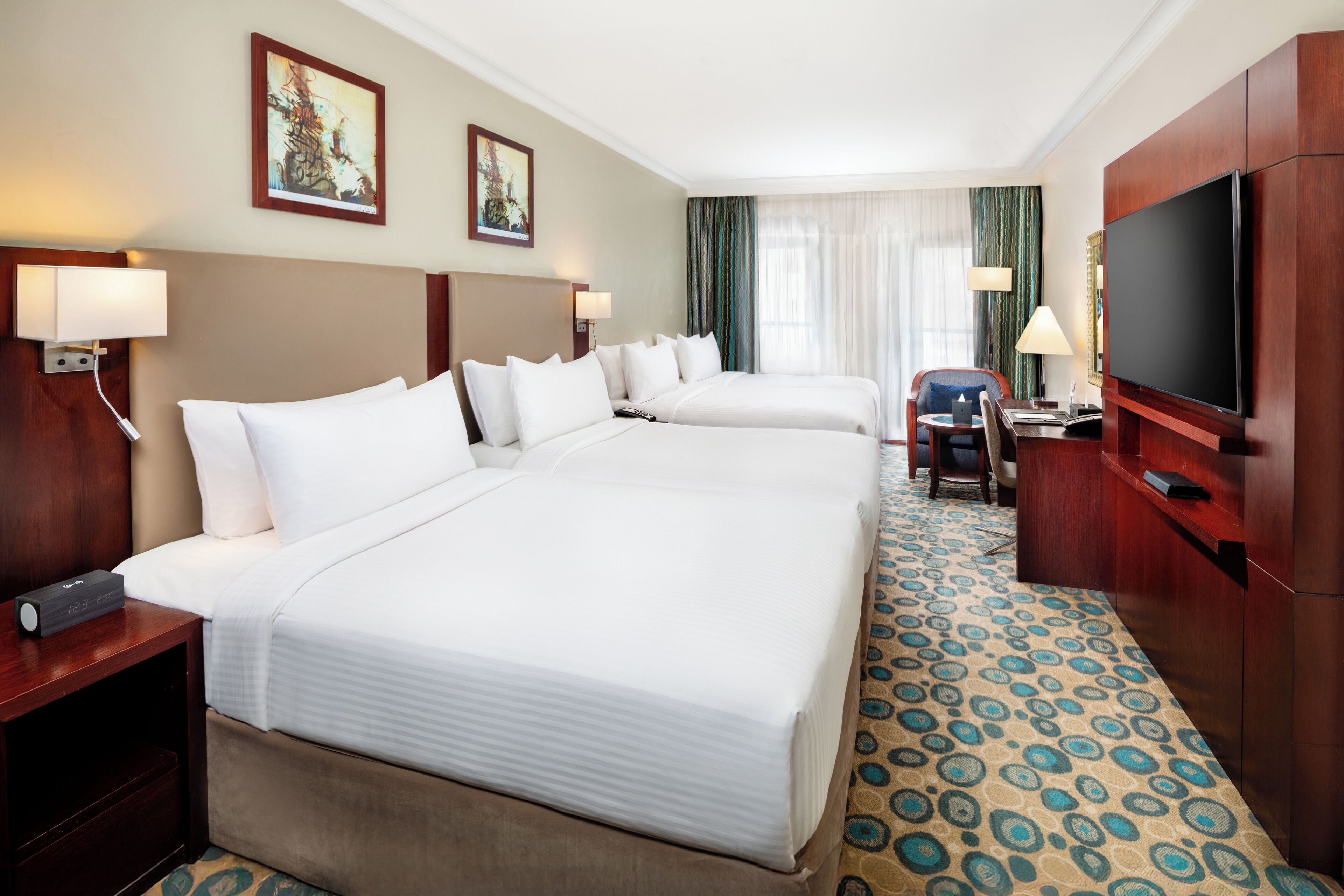 A hotel room with two beds, a desk with a chair, a TV, and artwork on the walls.