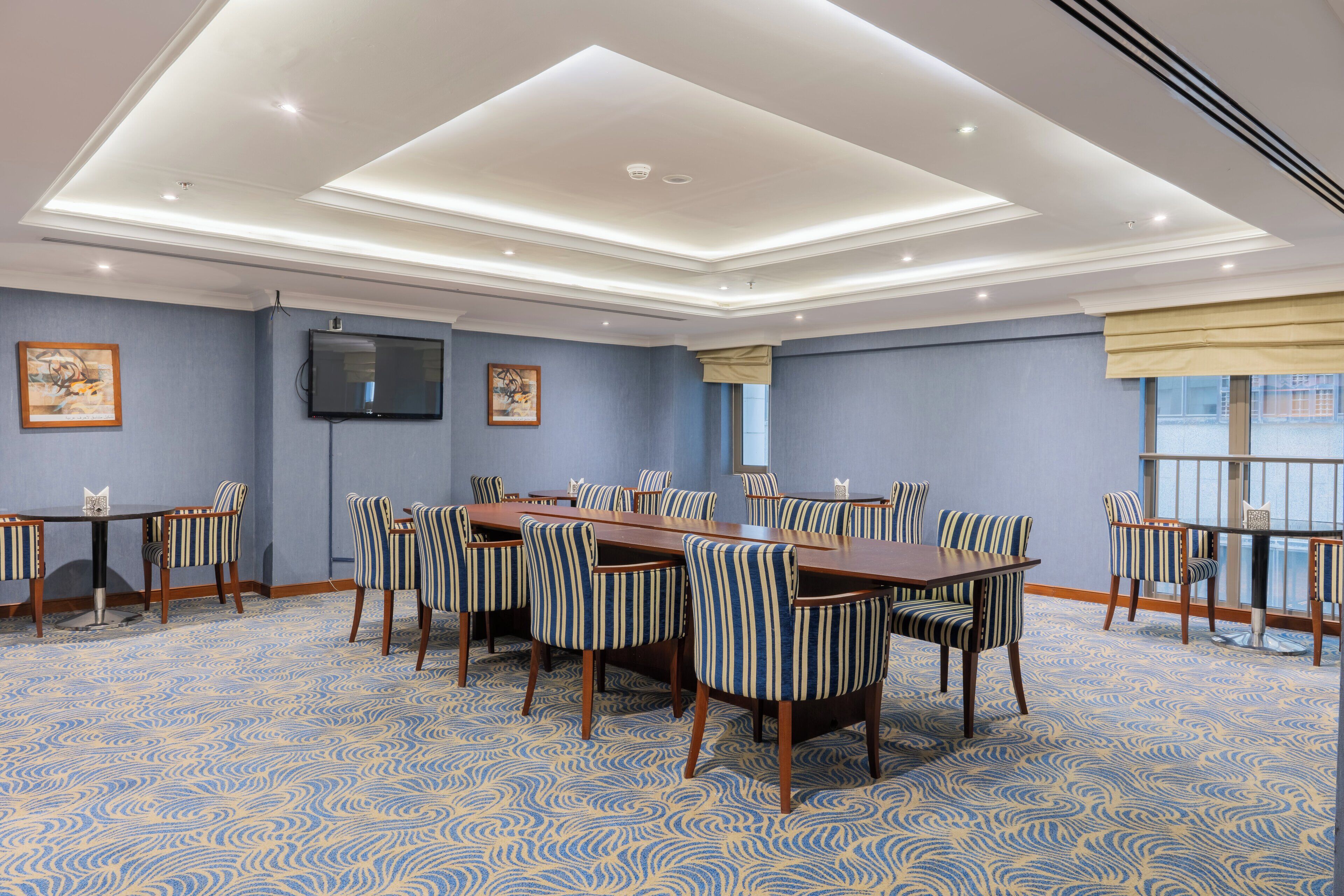 A conference room with a long table, striped chairs, a flat-screen TV, and patterned carpet.