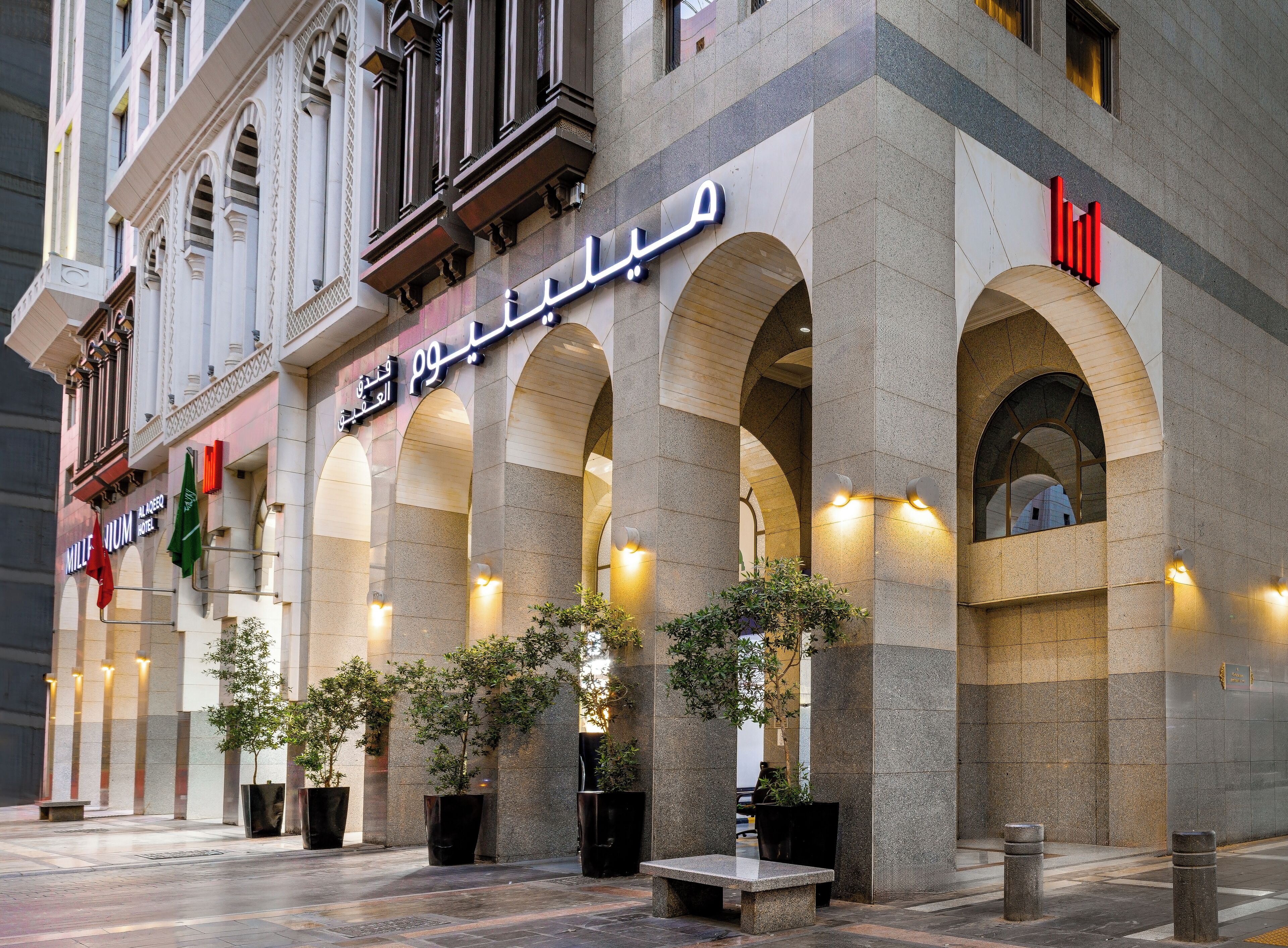 La façade d’un hôtel, ornée d’arcs en plein cintre, affiche une enseigne en arabe et un logo rouge.