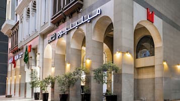 La façade d’un hôtel, ornée d’arcs en plein cintre, affiche une enseigne en arabe et un logo rouge.