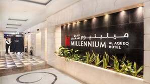 Het uiterlijk van Millennium Al Aqeeb Hotel, met een geruit vloerpatroon en een receptiegedeelte met een medewerker.