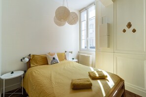 Une chambre à coucher bien aménagée, avec un grand lit, des tables de chevet, une fenêtre avec des stores et des éléments décoratifs sur les murs.