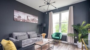 A modern living room with a grey sofa, a green armchair, a coffee table, and a cityscape painting on the wall. - Cozy New-Built Home in Downtown Atlanta (Atlanta)