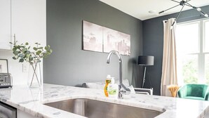 A modern kitchen with a large sink, a cityscape artwork on the wall, and a green chair in the background. - Cozy New-Built Home in Downtown Atlanta (Atlanta)