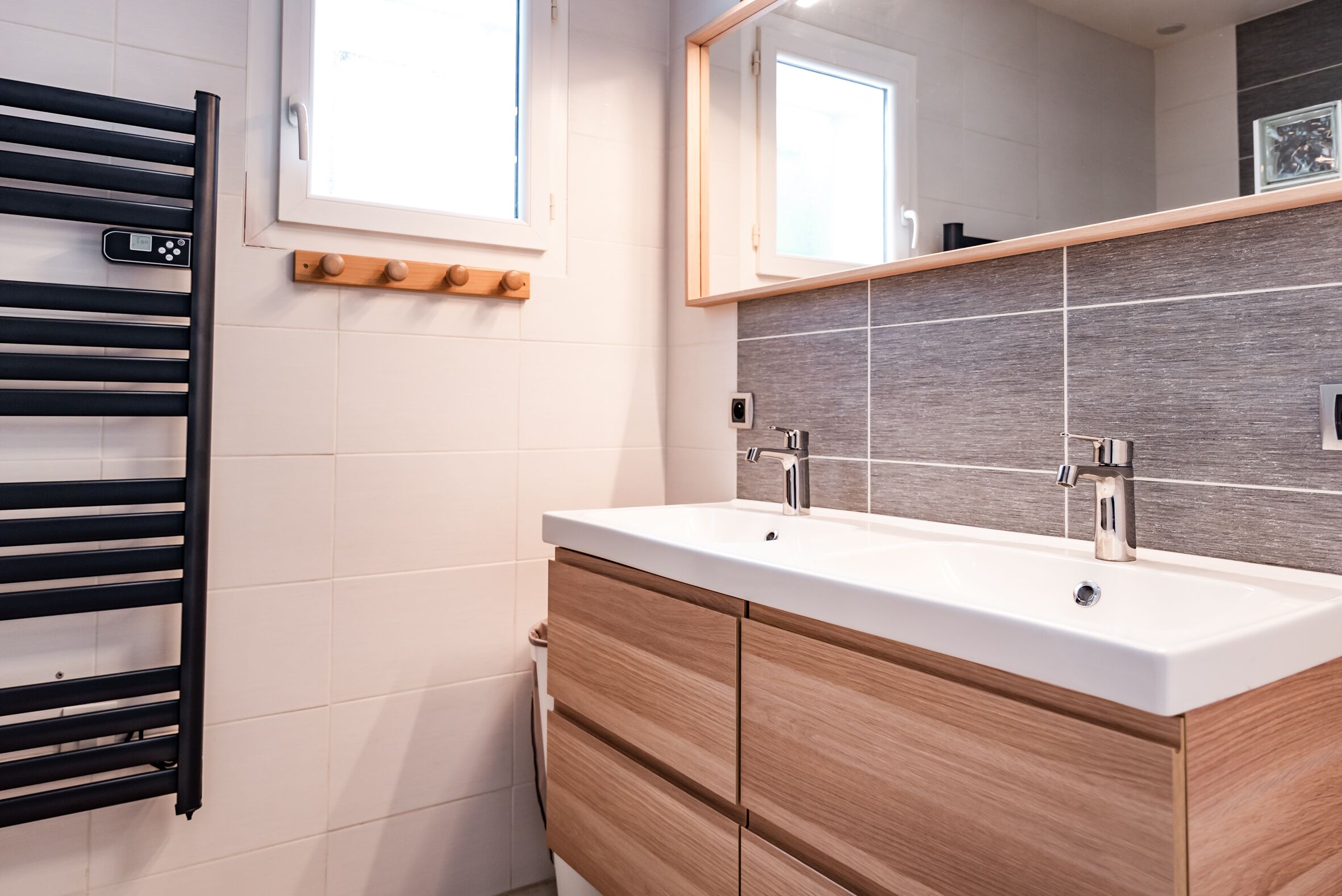 A modern bathroom with a white sink, wooden cabinets, a black towel rack, and a mirror above the sink.