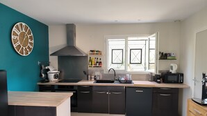 Una cocina moderna con una isla central, armarios negros, un extractor de acero inoxidable y una ventana con persianas abiertas.