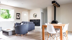 Una sala de estar moderna con un sofá gris, una mesa de comedor con sillas blancas, una chimenea y un gran ventanal con vistas a zonas verdes.
